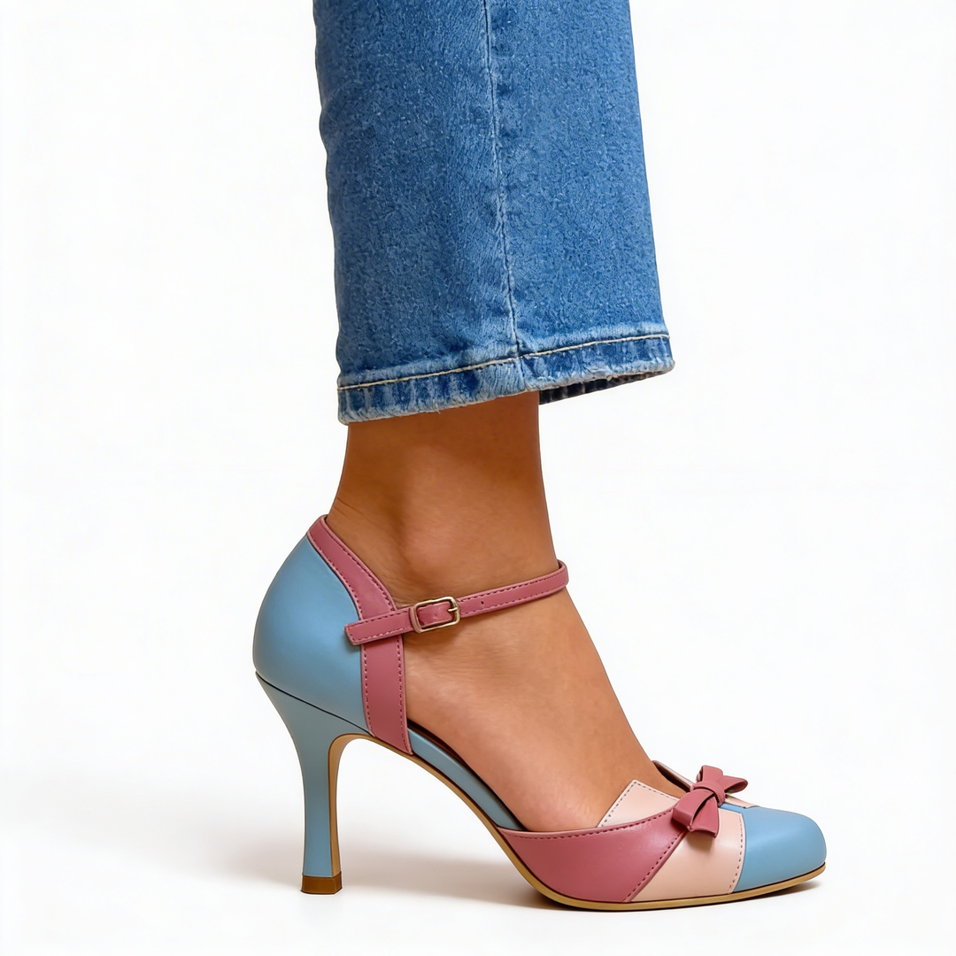 Womens retro bow accent colour block pumps featuring a rounded toe, ankle strap fastening, contrast panel detailing and high heel design